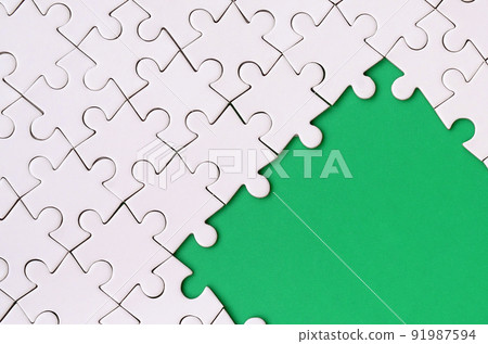 Fragment of a folded white jigsaw puzzle on the background of a green plastic surface. Texture photo with copy space for text Fragment of a folded white jigsaw puzzle on the background of a green plastic surface. Texture photo with copy space for text 91987594