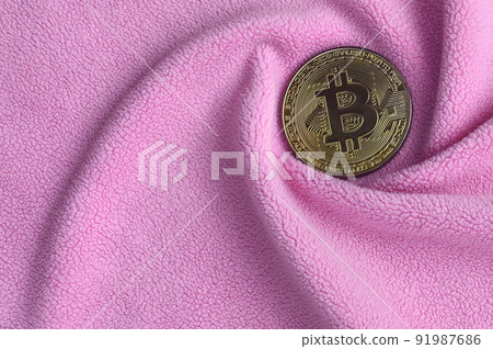 The golden bitcoin lies on a blanket made of soft and fluffy light pink fleece fabric with a large number of relief folds. The shape of the folds resembles a fan from a video card cooler 91987686