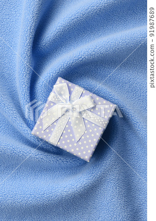 A small gift box in blue with a small bow lies on a blanket of soft and furry light blue fleece fabric with a lot of relief folds. Packing for a gift to your lovely girlfriend A small gift box in blue with a small bow lies on a blanket of soft and furry light blue fleece fabric with a lot of relief folds. Packing for a gift to your lovely girlfriend 91987689