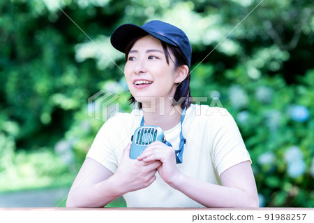 一位年輕女子在新鮮的綠色公園裡用便攜式風扇降溫 一位年輕女子在新鮮的綠色公園裡用便攜式風扇降溫 91988257