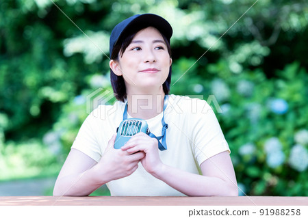 一位年輕女子在新鮮的綠色公園裡用便攜式風扇降溫 一位年輕女子在新鮮的綠色公園裡用便攜式風扇降溫 91988258