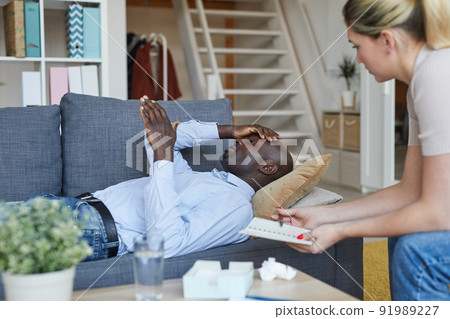 Confused young Afro-American man in shirt lying on sofa and gesturing hand while speaking about his problem, psychologist analyzing his words of patient and making notes in notepad 91989227