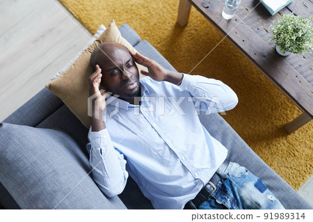 Above view of troubled young Afro-American man in shirt lying on psychiatrists couch and massaging temples at therapy session Above view of troubled young Afro-American man in shirt lying on psychiatrists couch and massaging temples at therapy session 91989314