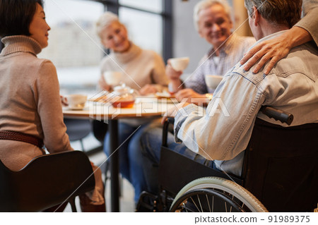 Group of senior people visiting friend in wheelchair: they drinking tea and chatting at home Group of senior people visiting friend in wheelchair: they drinking tea and chatting at home 91989375