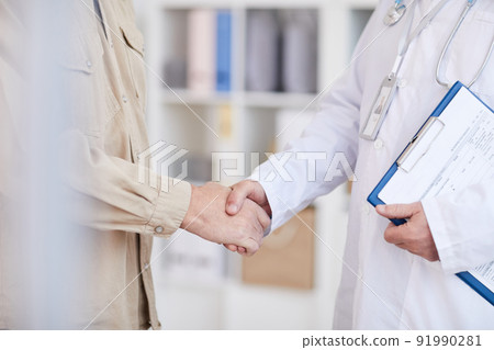 Close-up of unrecognizable man in casual shirt handshaking with doctor while meeting him in hospital 91990281