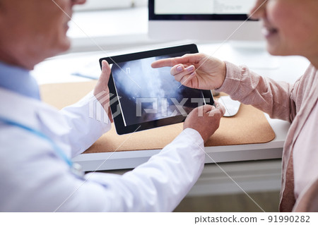 Close-up of female patient pointing at online x-ray image while discussing spinal problem with doctor at appointment 91990282