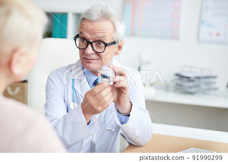 Content senior physician in eyeglasses frowning forehead while prescribing pills to patient at consultation 91990299