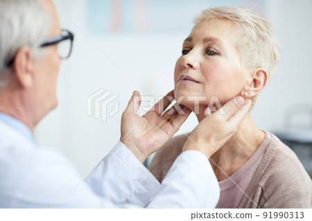 Over shoulder view of senior endocrinologist touching neck of mature female patient while examining her thyroid Over shoulder view of senior endocrinologist touching neck of mature female patient while examining her thyroid 91990313