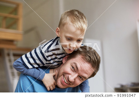 Happy little blond-haired boy climbing fathers neck while they playing active game at home 91991047
