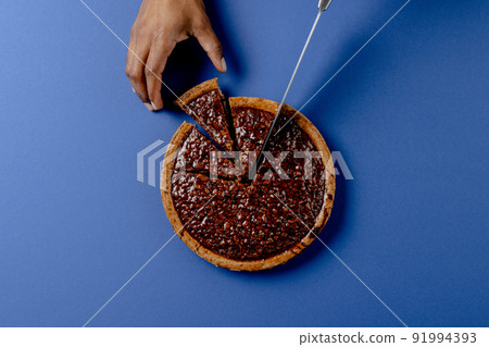 Composition of hands of biracial man cutting pie with knife on blue background Composition of hands of biracial man cutting pie with knife on blue background 91994393