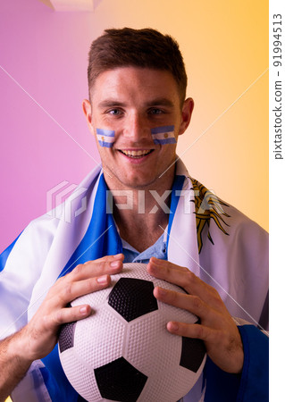 Portrait of happy caucasian male supporter with flag of argentina over pink lighting Portrait of happy caucasian male supporter with flag of argentina over pink lighting 91994513