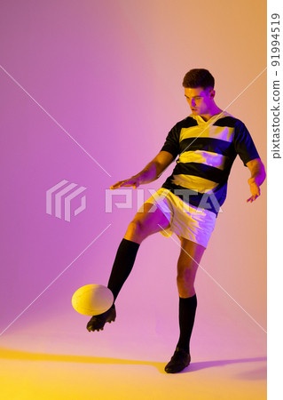 Caucasian male rugby player kicking rugby ball over pink lighting 91994519