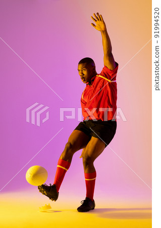 African american male rugby player kicking rugby ball over pink lighting 91994520
