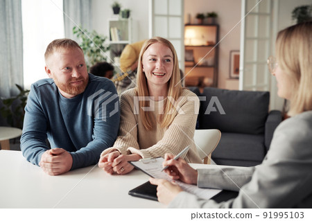 Happy foster couple answering questions from social worker at table during their meeting at home Happy foster couple answering questions from social worker at table during their meeting at home 91995103