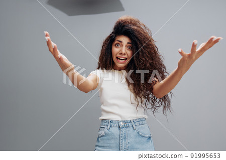 Close up shot of surprised terrific young lady stares with eyes popped out, notices something terrible in front, spreading hands at camera, posing isolated at gray background. People emotions concept Close up shot of surprised terrific young lady stares with eyes popped out, notices something terrible in front, spreading hands at camera, posing isolated at gray background. People emotions concept 91995653