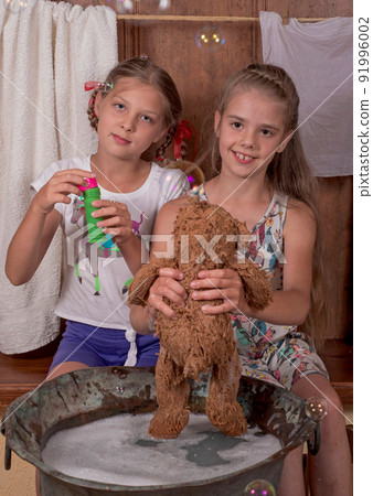 Little girlfriends. Cute happy girls bathe teddy bears, blow bubbles. 91996002