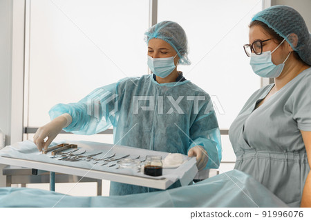 Doctor and nurse examining table with surgical instruments before the operation Doctor and nurse examining table with surgical instruments before the operation 91996076