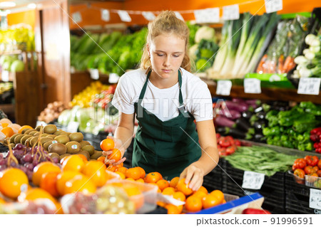 Fifteen-year-old girl who works part-time as a trainee saleswoman puts tangerines 91996591