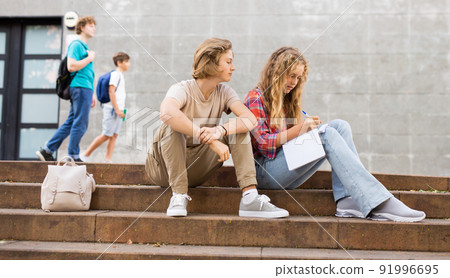 Guy helps girl to solve the school problem while sitting on stone stairs in front of school 91996695