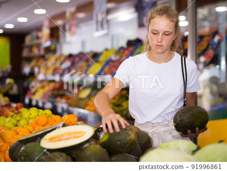 Focused fifteen-year-old girl chooses a ripe melon Focused fifteen-year-old girl chooses a ripe melon 91996861