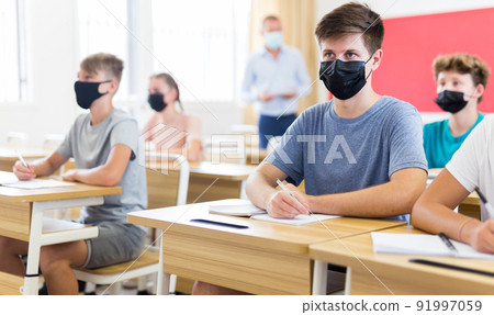 Teenager in protective mask writing in workbook on lesson 91997059