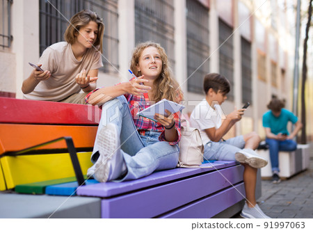 Group of teenagers sitting on bench outdoors 91997063