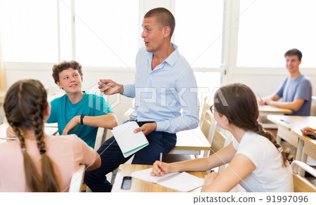 Male teacher working with teen students in classroom at school 91997096