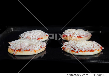 Four uncooked mini pizzas on tray in electric oven: front view, black background Four uncooked mini pizzas on tray in electric oven: front view, black background 91998469