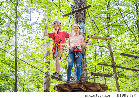 Mother and son climbing in extreme road trolley zipline in forest on carabiner safety link on tree to tree top rope adventure park. Family weekend children kids activities concept 91998487