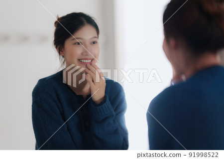 Portrait of Young Asian woman looking in mirror checking her face at bathroom. Lifestyle concept. Portrait of Young Asian woman looking in mirror checking her face at bathroom. Lifestyle concept. 91998522
