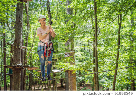 Happy women girl female gliding climbing in extreme road trolley zipline in forest on carabiner safety link on tree to tree top rope adventure park. Family weekend children kids activities concept 91998549