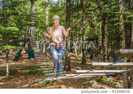 Happy women girl female gliding climbing in extreme road trolley zipline in forest on carabiner safety link on tree to tree top rope adventure park. Family weekend children kids activities concept 91998650