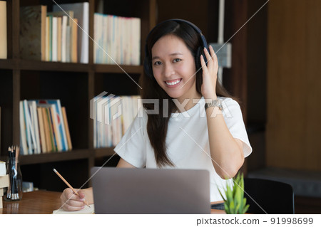 Image of Young woman with a headset working online on laptop computer. studying or working from home online concept. Image of Young woman with a headset working online on laptop computer. studying or working from home online concept. 91998699