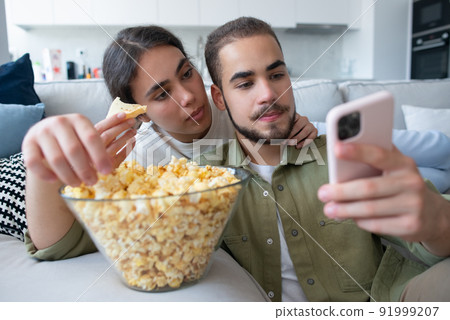 Happy couple eating popcorn and watching movie 91999207