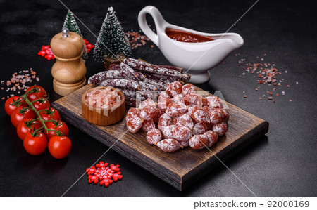Delicious dry sausage with walnuts on a christmas table. Dry cured fuet sausage on a dark background Delicious dry sausage with walnuts on a christmas table. Dry cured fuet sausage on a dark background 92000169