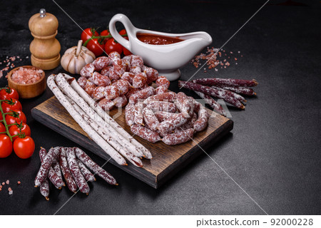 Delicious dry sausage with walnuts on a concrete table. Dry cured fuet sausage on a dark background Delicious dry sausage with walnuts on a concrete table. Dry cured fuet sausage on a dark background 92000228
