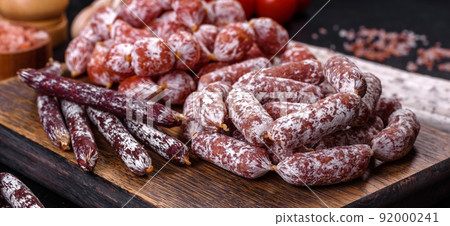 Delicious dry sausage with walnuts on a concrete table. Dry cured fuet sausage on a dark background Delicious dry sausage with walnuts on a concrete table. Dry cured fuet sausage on a dark background 92000241