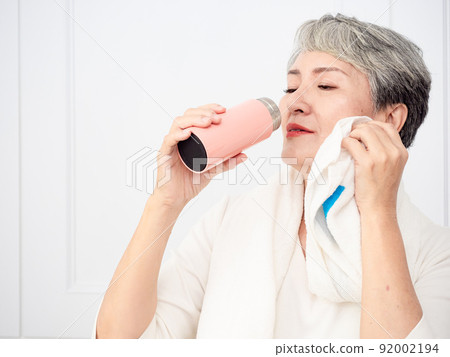 披著運動毛巾的成熟50多歲亞洲女人運動後拿著水瓶的肖像 92002194