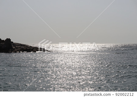 擁有閃閃發光的海面、岩石碼頭、地平線和朦朧的藍天的景觀 擁有閃閃發光的海面、岩石碼頭、地平線和朦朧的藍天的景觀 92002212