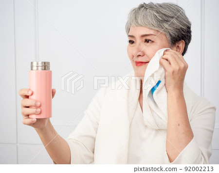 披著運動毛巾的成熟50多歲亞洲女人運動後拿著水瓶的肖像 92002213