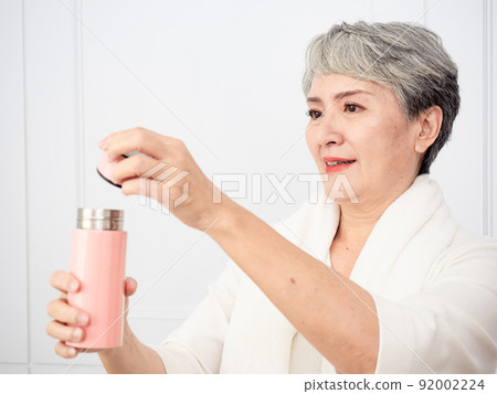 披著運動毛巾的成熟50多歲亞洲女人運動後拿著水瓶的肖像 92002224