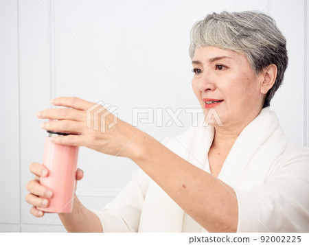 披著運動毛巾的成熟50多歲亞洲女人運動後拿著水瓶的肖像 92002225