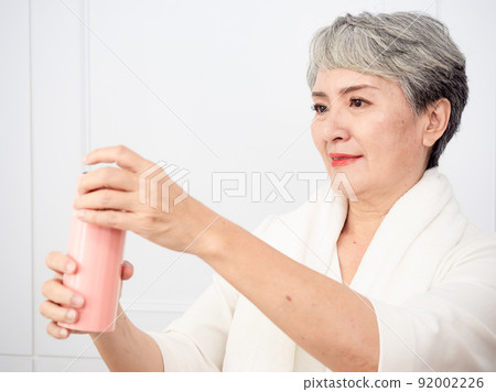 披著運動毛巾的成熟50多歲亞洲女人運動後拿著水瓶的肖像 披著運動毛巾的成熟50多歲亞洲女人運動後拿著水瓶的肖像 92002226