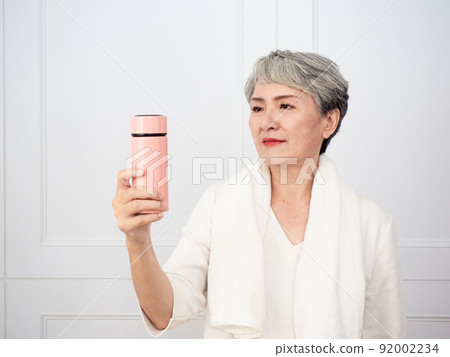 披著運動毛巾的成熟50多歲亞洲女人運動後拿著水瓶的肖像 92002234