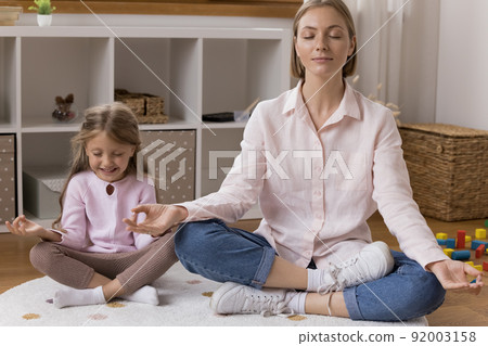 Cheerful little daughter kid and calm young mother meditating together 92003158