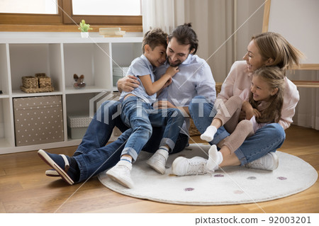 Joyful happy young parents cuddling, tickling two excited giggling kids Joyful happy young parents cuddling, tickling two excited giggling kids 92003201