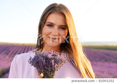 Young woman in dress holding bouquet of flowers standing in lavender field Young woman in dress holding bouquet of flowers standing in lavender field 92003202