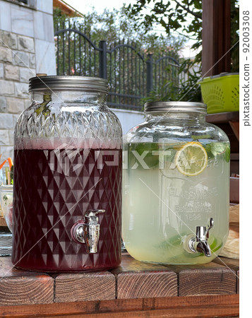 Glass jar of lemonade next to a jar of cherry juice stands on the table Glass jar of lemonade next to a jar of cherry juice stands on the table 92003308