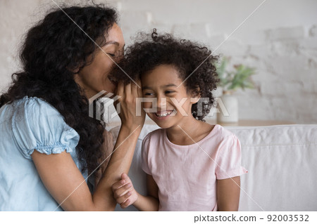 Young mom whispering in ear share secret to smiling daughter 92003532