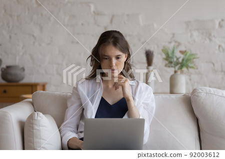 Pensive young freckled woman studying or working using laptop Pensive young freckled woman studying or working using laptop 92003612